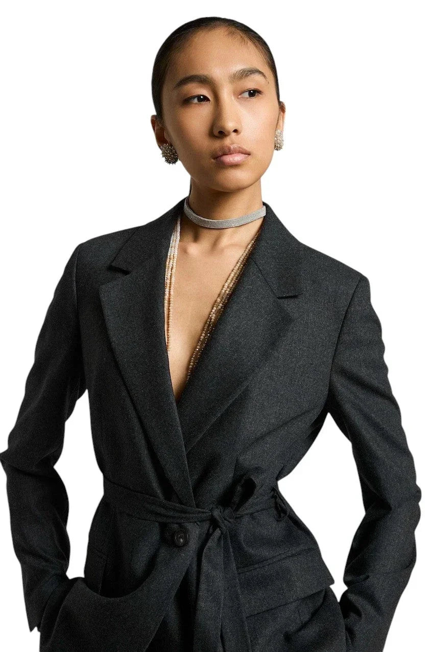 Vrouw in een elegante donkergrijze blazer met tailleband en sieraden.