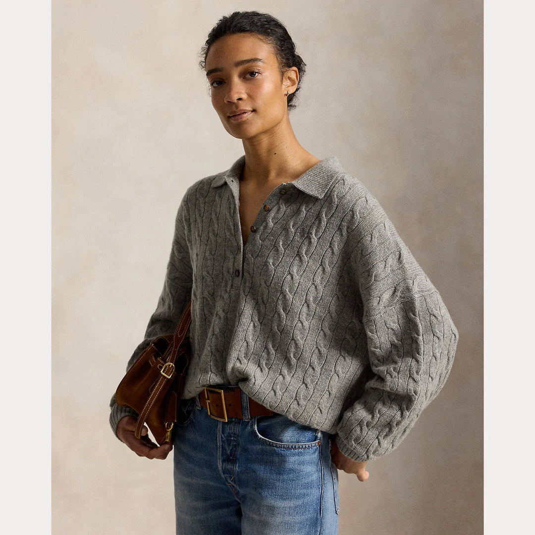 Vrouw in een grijze kabelgebreide cardigan met kraag en een blauwe spijkerbroek.